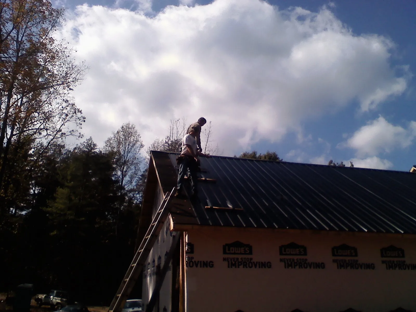 Roofer fastening dark metal panels high against a cloudy sky, from a Roof Inspection job in Darby