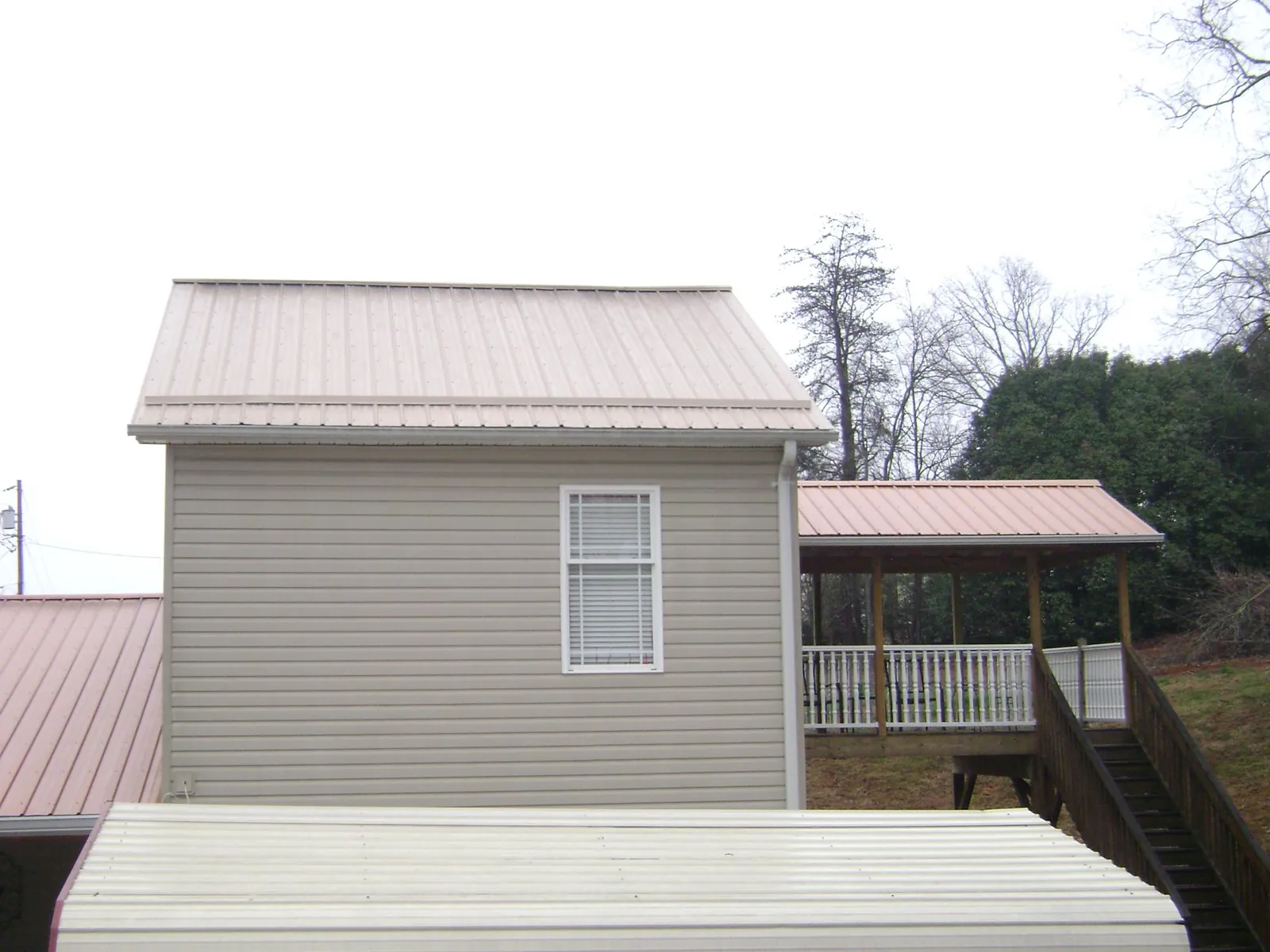 Tan metal roofs on a two story addition and attached porch, from a Roof Replacement job in Darby